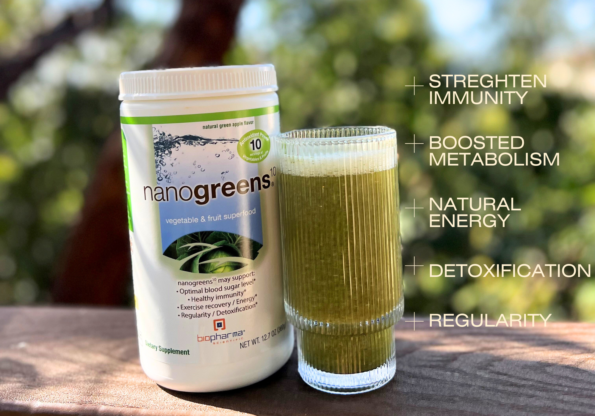 Nanogreens supplement bottle with a glass of green juice on a wooden surface, outdoors.